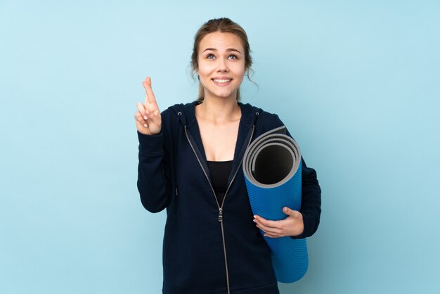 Chica adolescente sosteniendo estera en azul con los dedos cruzando