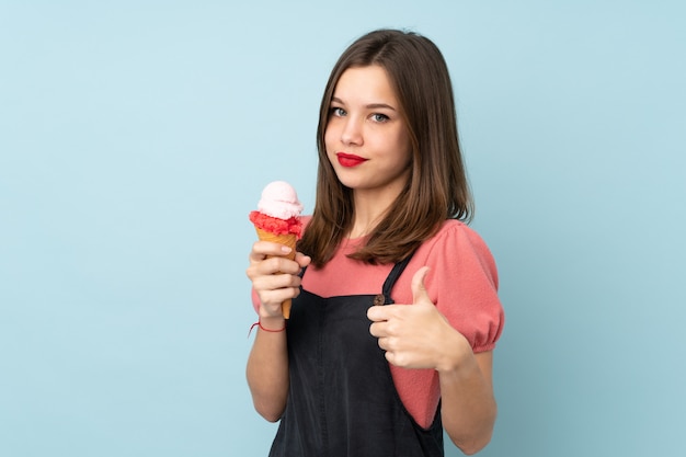 Chica adolescente sosteniendo un helado de cucurucho en azul con los pulgares hacia arriba porque algo bueno ha sucedido