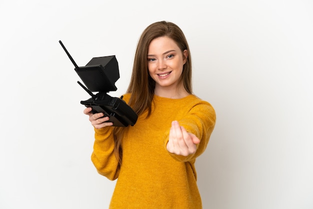 Chica adolescente sosteniendo un teledirigido drone sobre fondo blanco aislado que invita a venir con la mano. Feliz de que hayas venido