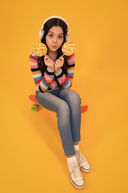 Chica adolescente sostiene caramelo de piruleta en la tienda de dulces de fondo amarillo