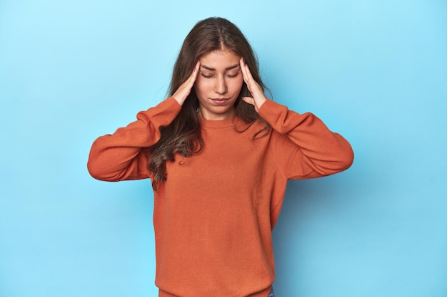 Chica adolescente con suéter naranja vibrante en azul tocando las sienes y teniendo dolor de cabeza