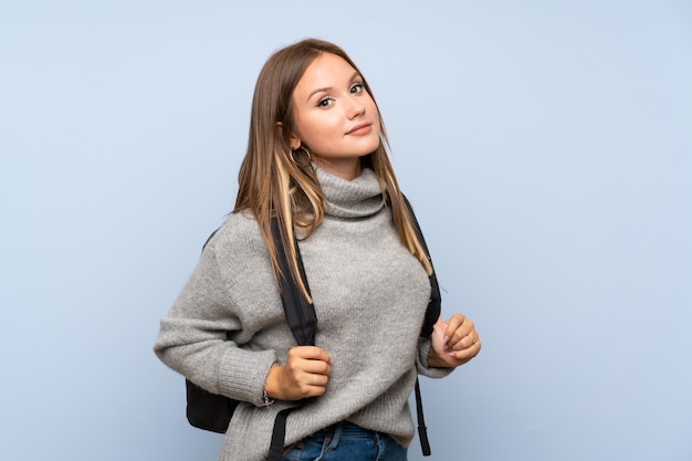 Chica adolescente con suéter sobre pared azul aislada con mochila