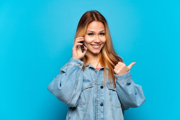 Chica adolescente mediante teléfono móvil sobre antecedentes aislados apuntando hacia el lado para presentar un producto