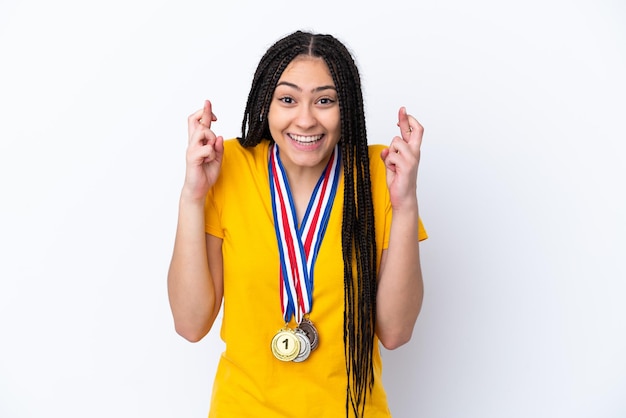 Foto chica adolescente con trenzas y medallas sobre fondo rosa aislado con los dedos cruzados