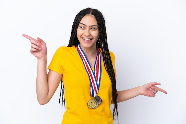 Chica adolescente con trenzas y medallas sobre fondo rosa aislado señalando con el dedo a los laterales y feliz