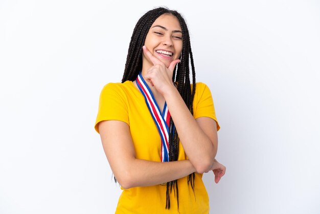 Chica adolescente con trenzas y medallas sobre fondo rosa aislado sonriendo