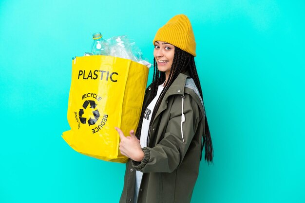 Chica adolescente con trenzas sosteniendo una bolsa para reciclar apuntando hacia atrás