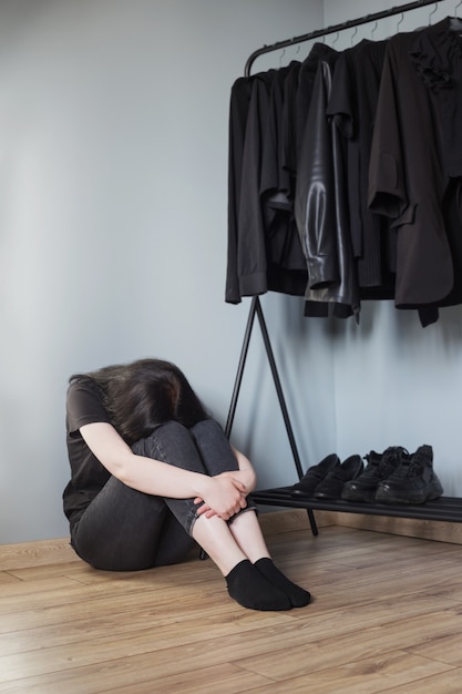 Chica adolescente triste en jeans negros y una camiseta cerca de la percha con ropa negra