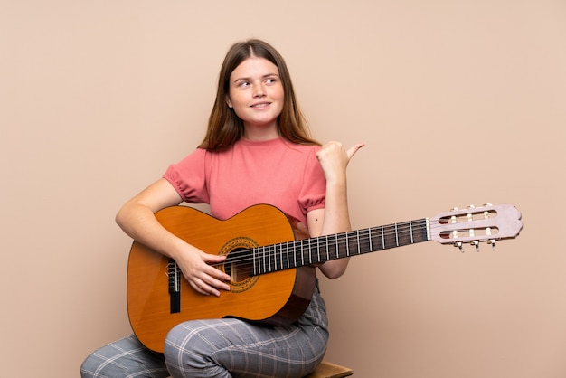 Chica adolescente ucraniana con guitarra sobre aislado apuntando hacia el lado para presentar un producto