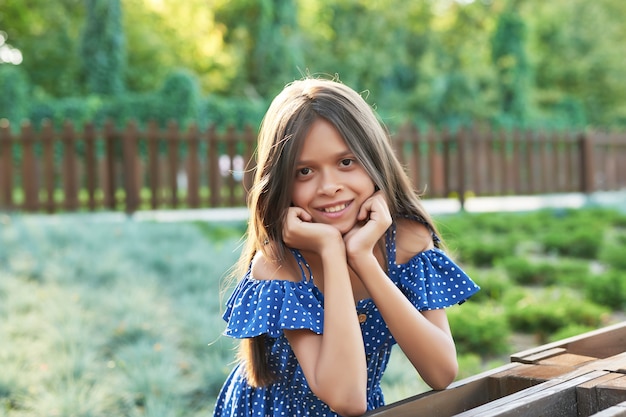 Chica adolescente con un vestido azul camina en el parque de verano al atardecer