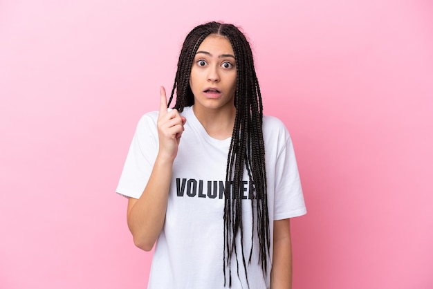 Chica adolescente voluntaria con trenzas aisladas sobre fondo rosa con la intención de darse cuenta de la solución mientras levanta un dedo