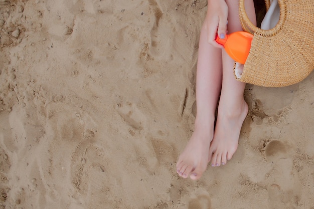 Chica en aerosol de aceite bronceado sus piernas protección de los rayos ultravioleta del sol poniendo bloqueador solar loción de protección solar