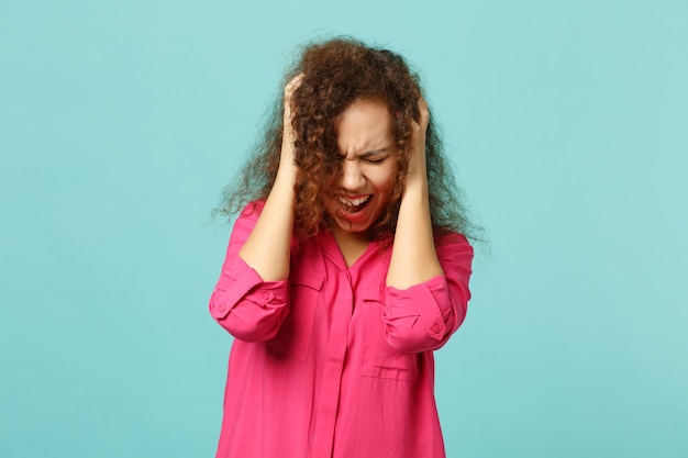 Foto chica africana gritando en ropa casual manteniendo los ojos cerrados, poniendo las manos en la cabeza aislada sobre fondo azul turquesa en estudio. personas sinceras emociones, concepto de estilo de vida. simulacros de espacio de copia.