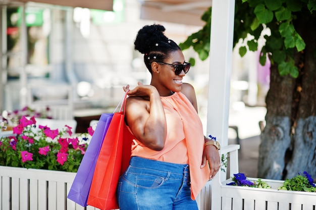 Chica afroamericana casual con bolsas de colores caminando al aire libre. Elegante mujer negra de compras.