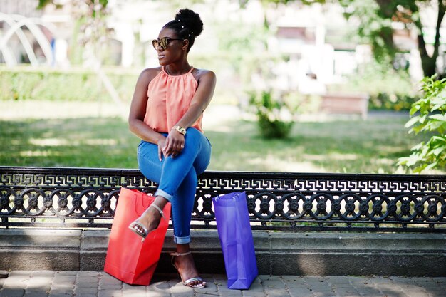 Chica afroamericana casual con bolsas de compras de colores caminando al aire libre Elegante mujer negra de compras