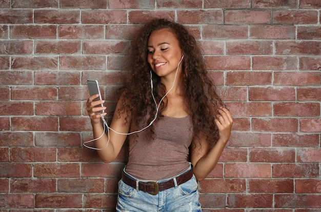 Chica afroamericana escuchando música en la pared de ladrillo