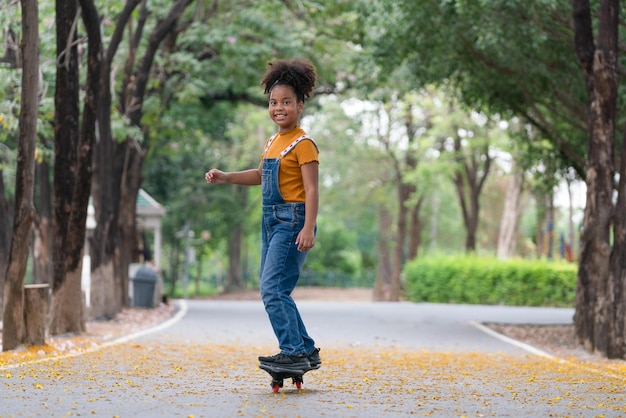 Chica afroamericana feliz jugando patineta en el parque Deporte al aire libre para niños