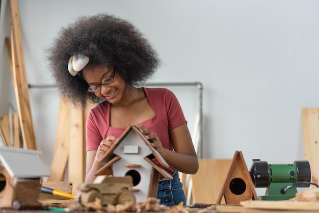 Chica afroamericana haciendo casa de pájaros de madera en el taller