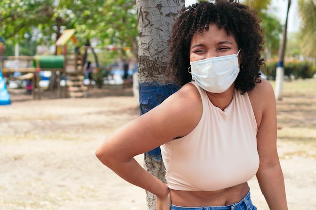 Chica afroamericana con una máscara protectora y de pie en el parque.