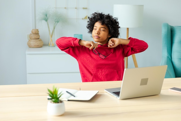 Chica afroamericana en la oficina en casa relajándose estirando las manos y el cuerpo tomando un descanso del trabajo en la