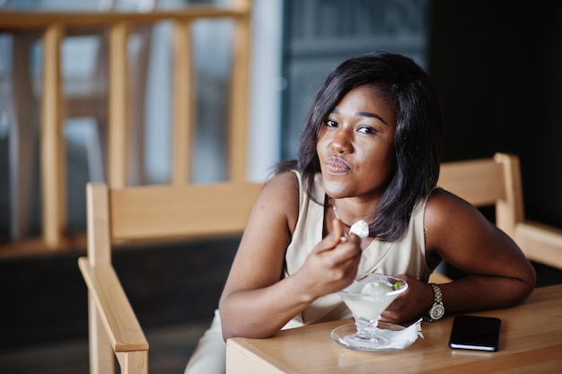 Chica afroamericana sentada en el café y comiendo helado