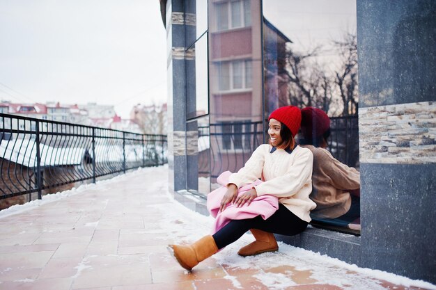 Chica afroamericana con sombrero rojo y abrigo rosa en la calle de la ciudad contra la construcción el día de invierno