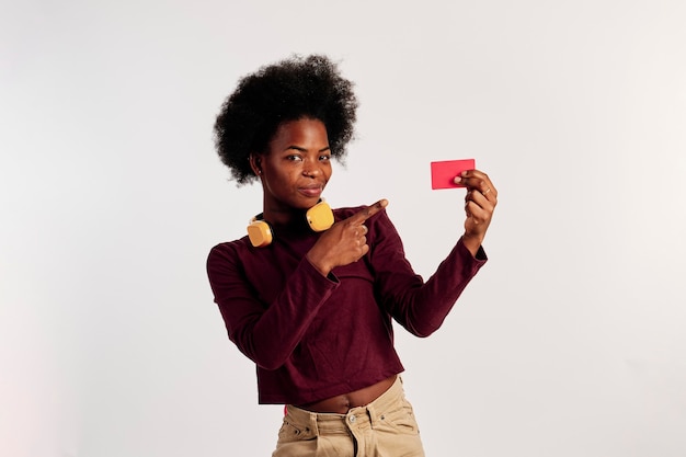 Chica afroamericana en suéter marrón posa mientras muestra su tarjeta de crédito.