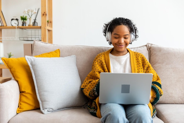 Chica afroamericana usando una computadora portátil en la oficina en casa mirando la pantalla escribiendo chateando leyendo escribiendo