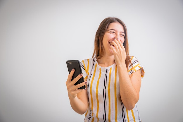 Chica aislada sobre fondo blanco usa su teléfono inteligente y se ríe Imagen de publicidad fotográfica de Studio