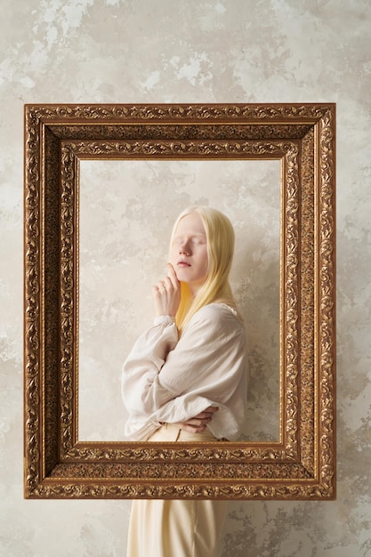 Chica albina joven en traje blanco de pie detrás del marco de imagen