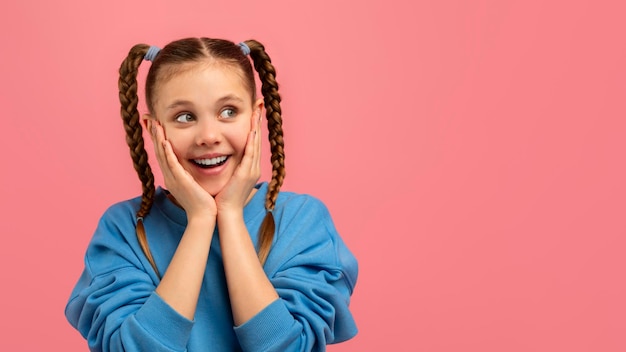 Chica alegre abrazando la cara con las manos sobre un fondo rosado