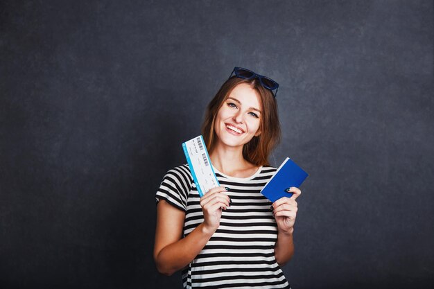 Chica alegre con billete de avión de pasaporte y globo terráqueo antes del concepto de viaje interior de fondo gris