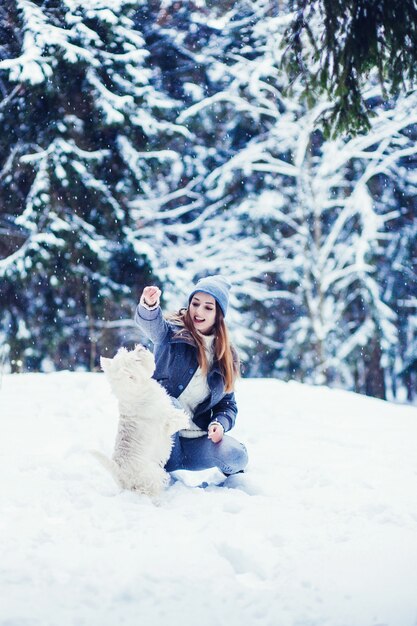 Chica alegre en el bosque de invierno jugando con su perro