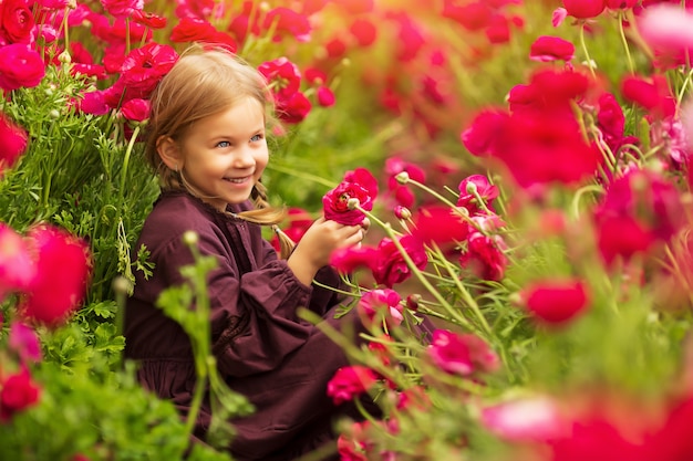 Chica alegre entre brillantes flores de primavera de ranúnculos