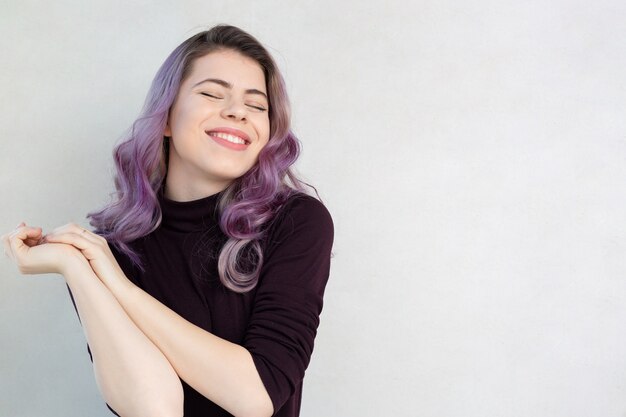 Chica alegre con cabello morado sobre un fondo gris. Espacio para texto