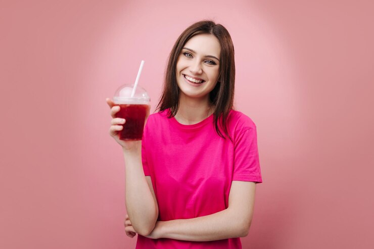 Chica alegre en camiseta rosa con cóctel fresco frío
