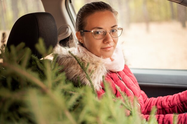 Chica alegre en el coche con un árbol de navidad