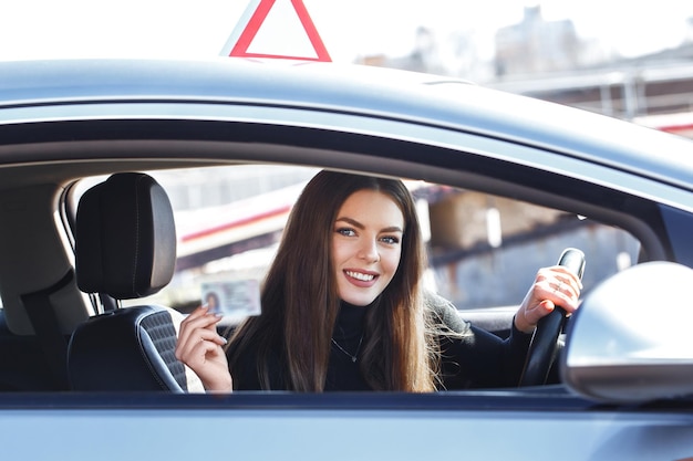 Foto chica alegre conduciendo un coche de entrenamiento con una tarjeta de licencia de conducir en sus manos.