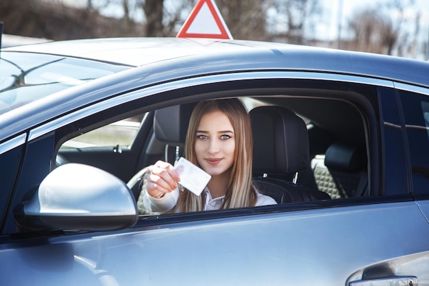 Chica alegre conduciendo un coche de entrenamiento con una tarjeta de licencia de conducir en sus manos.