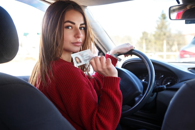 Chica alegre conduciendo un coche de entrenamiento con una tarjeta de licencia de conducir en sus manos.