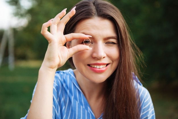 Chica alegre con dientes blancos sanos, sonriendo y mostrando un anillo.