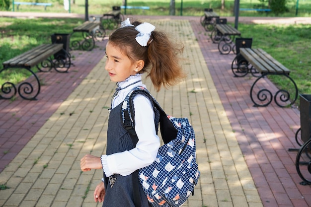 Chica alegre y divertida con una sonrisa desdentada en uniforme escolar con lazos blancos en el patio de la escuela Regreso a la escuela 1 de septiembre Alumno feliz con una mochila Clase primaria de educación primaria