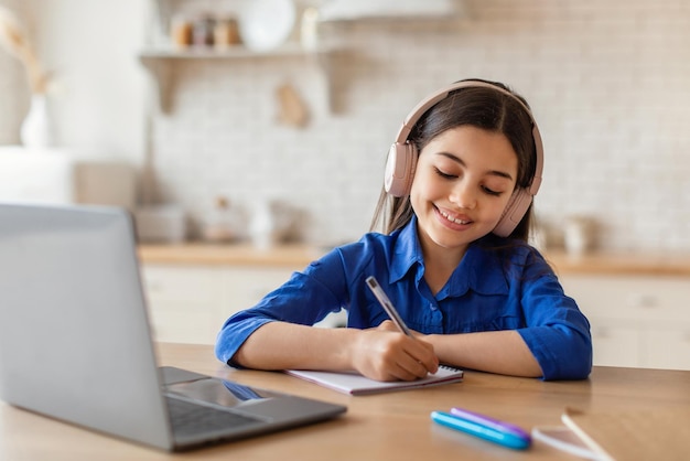 Chica alegre estudiando en línea usando una computadora portátil y auriculares en interiores