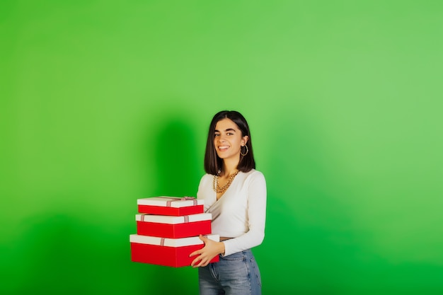 Chica alegre y feliz mantenga cajas de regalo, sonriendo emocionada. Ella celebrando cumpleaños y posando sobre superficie verde.