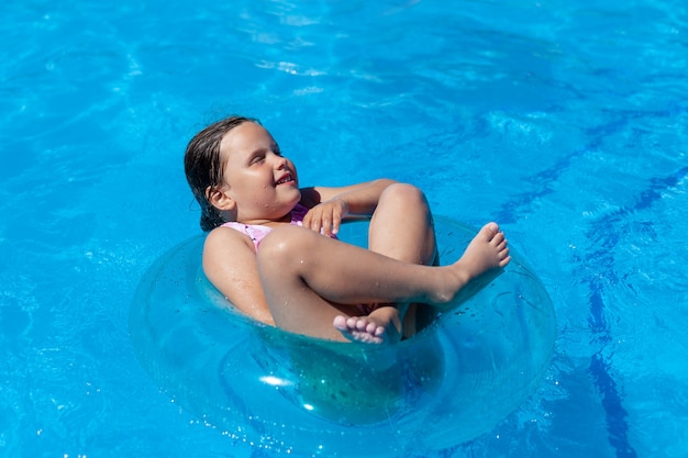 Chica alegre flotando con las piernas cruzadas y los ojos cerrados en un círculo inflable azul en la piscina del hotel en ...