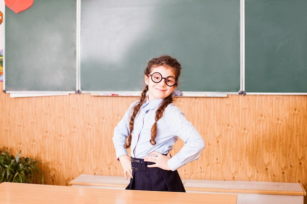 La chica alegre de las gafas está de pie en el aula