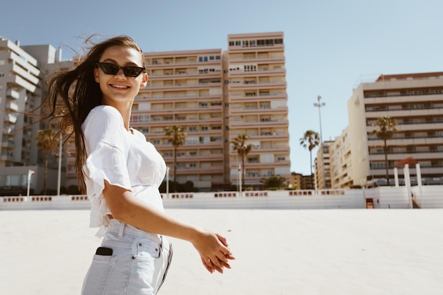 Chica alegre en gafas de sol en la playa con el telón de fondo de los edificios residenciales