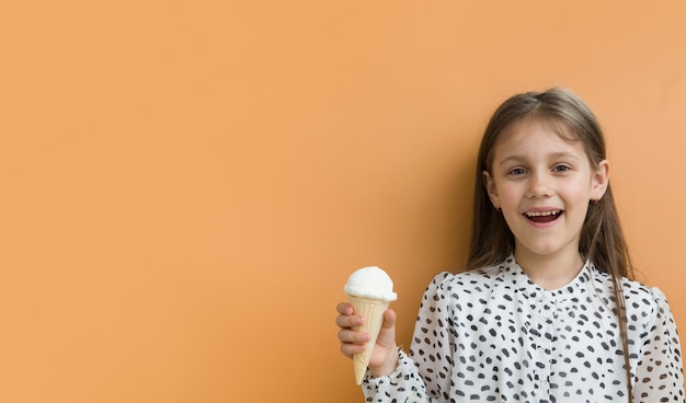 Chica alegre con helado en un cono sobre un fondo naranja con espacio de copia. Formato de banner