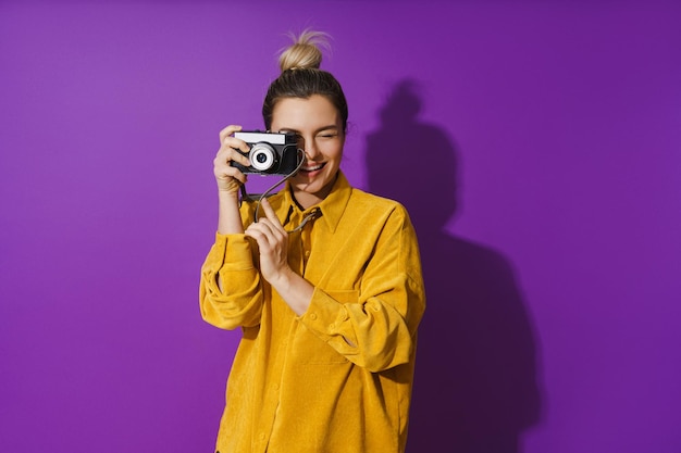 Chica alegre joven con cámara de fotos de película sobre fondo púrpura