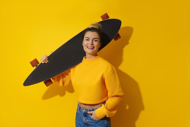 Chica alegre joven con longboard contra fondo amarillo